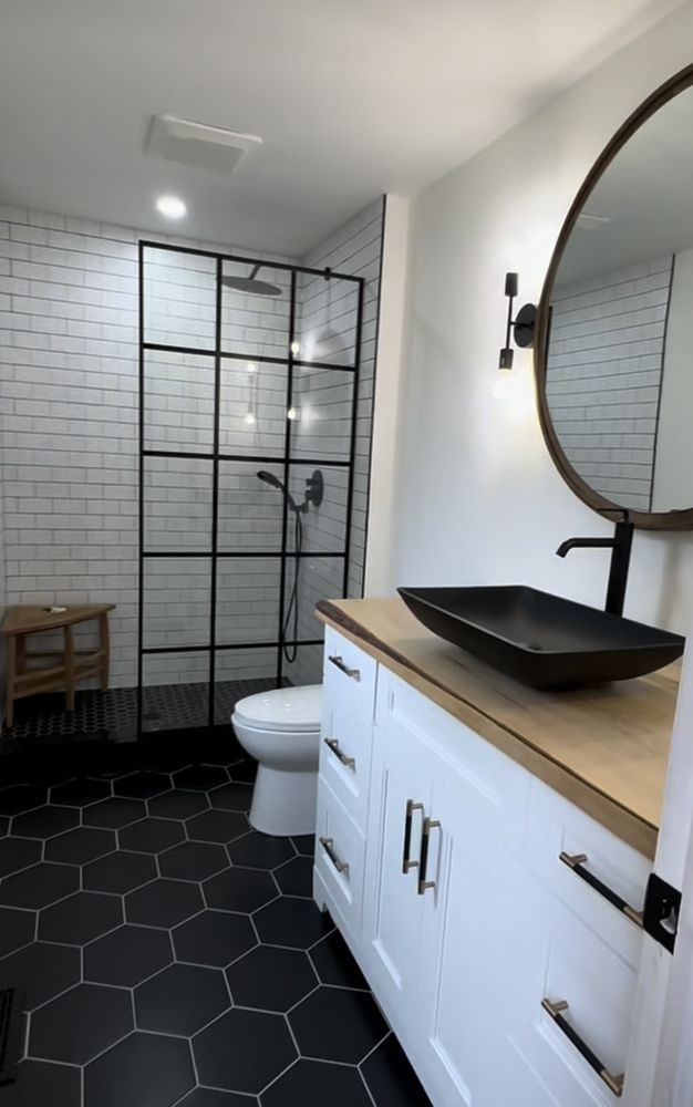Renovated bathroom with a black grid shower screen, white subway tile, black hexagon floor and a live-edge wood vanity top