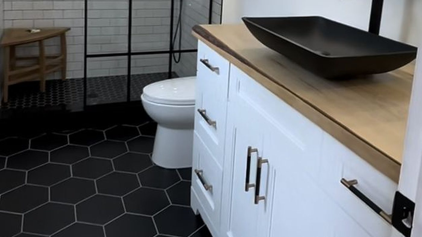 Renovated bathroom with a black grid shower screen, white subway tile, black hexagon floor and a live-edge wood vanity top