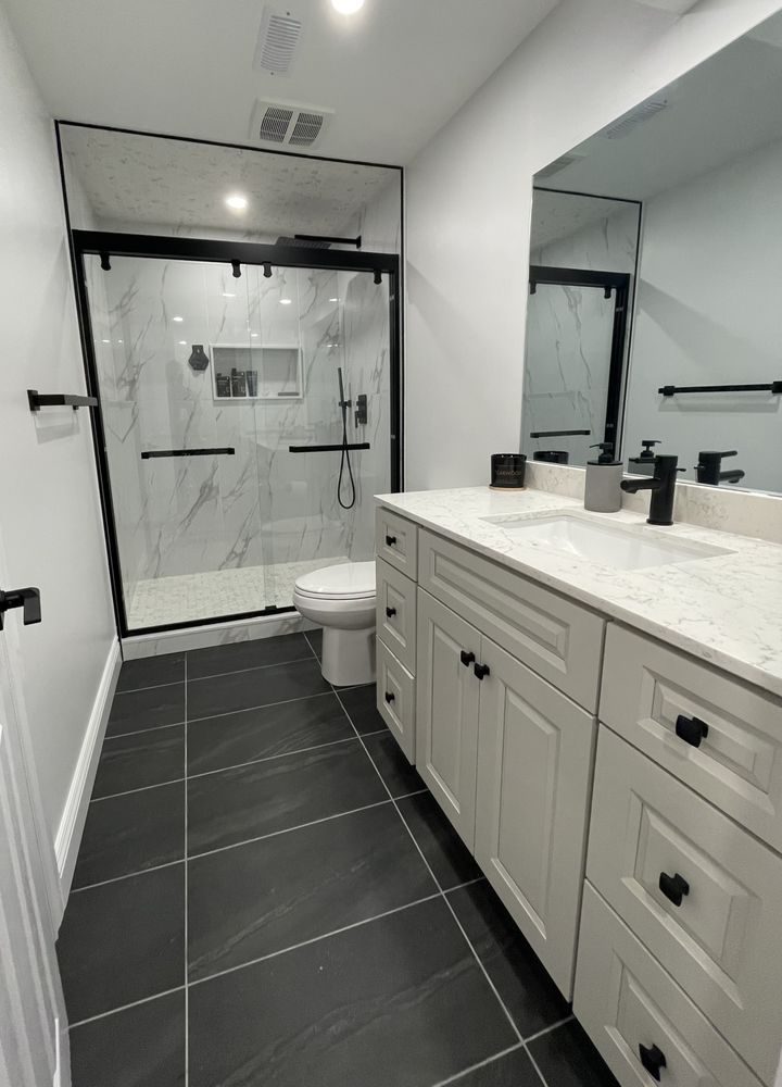 Renovated bathroom with a marble-look glass shower, quartz-topped shaker vanity and dark slate floor tile