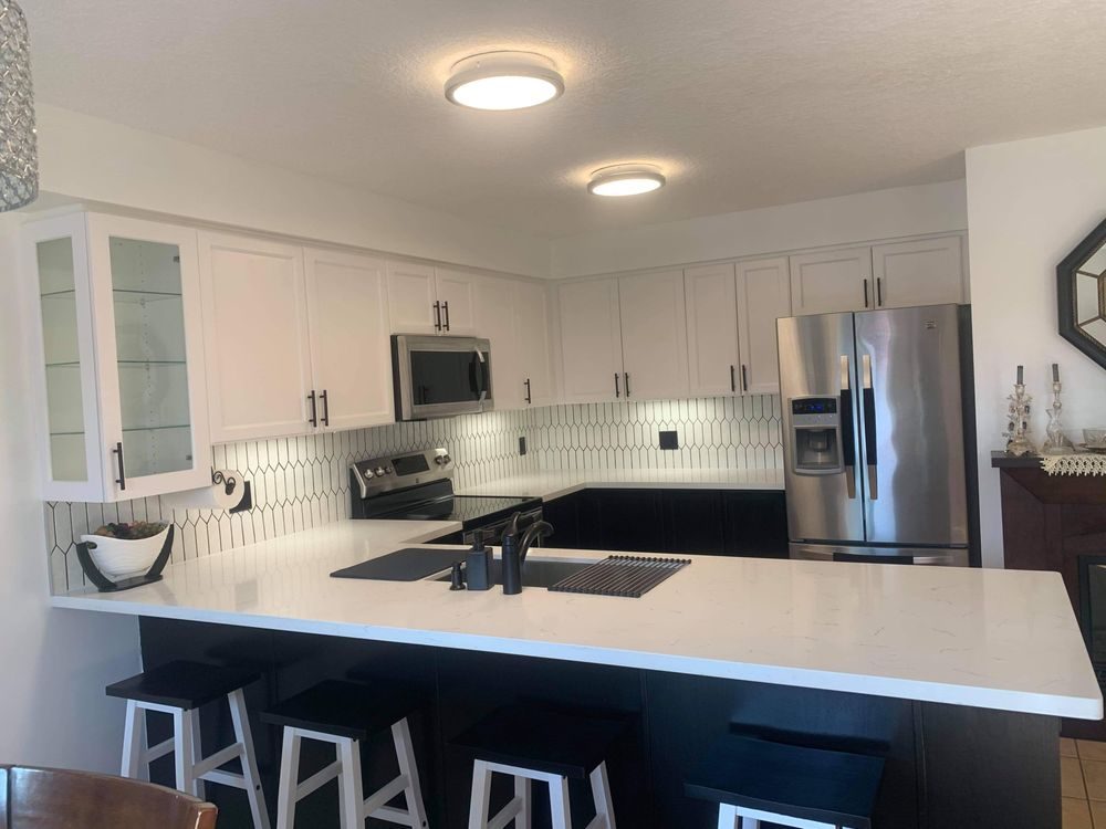 Renovated kitchen with white shaker upper cabinets, dark base cabinets and a white quartz peninsula