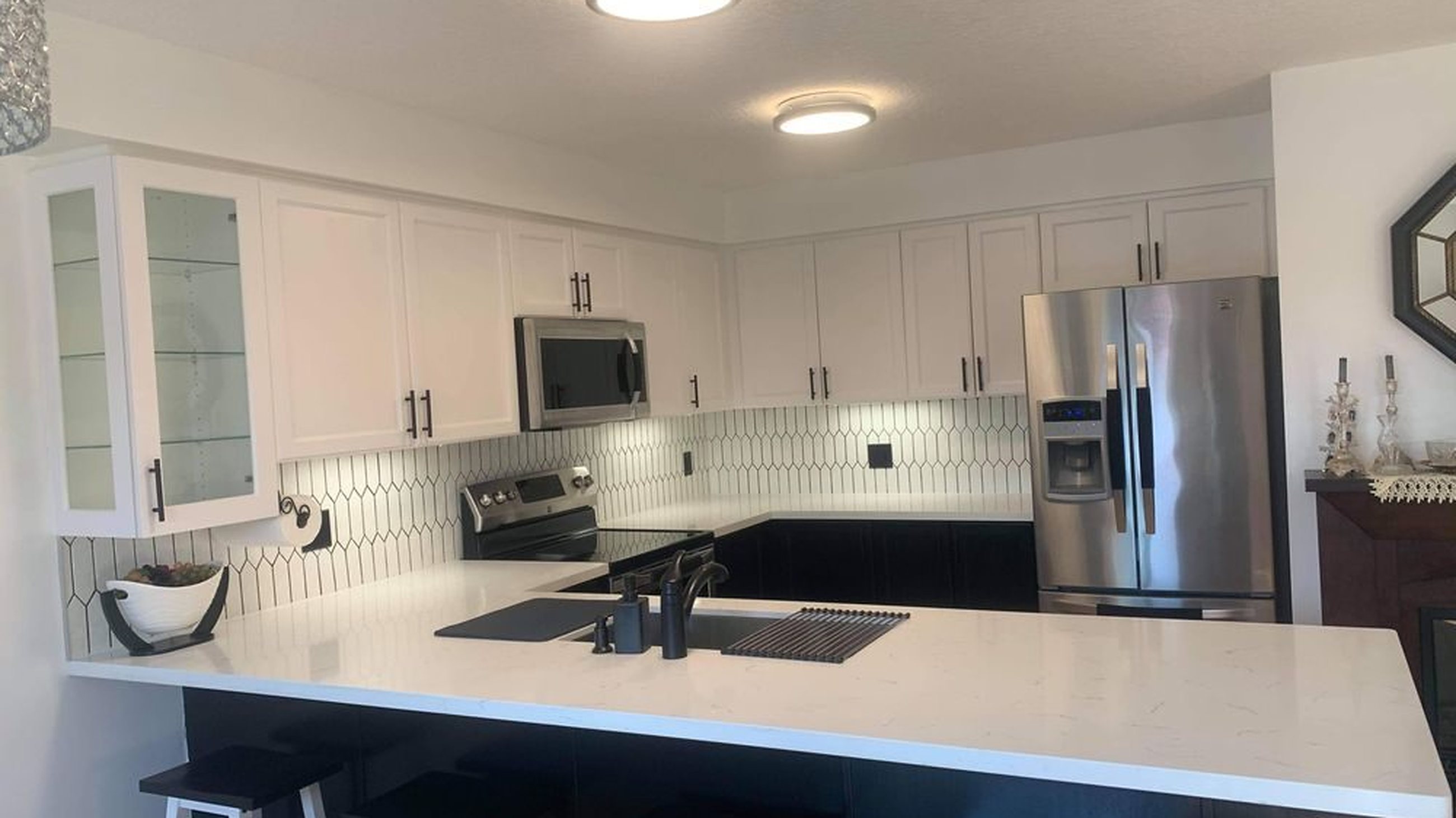 Renovated kitchen with white shaker upper cabinets, dark base cabinets and a white quartz peninsula